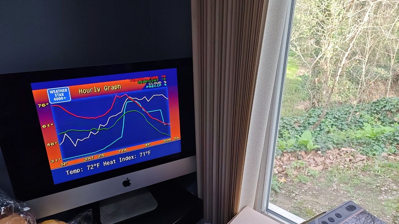 an iMac showing a WeatherStar4000+ display next to a window showing green foliage